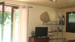 A room with a television on a wooden stand, a fan, and a shelf with decorative items. - between the sea and the Caribbean sun garden (Trinité)