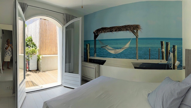 A bedroom with a large bed, a view of the sea through a window, and a hammock on a wooden deck.