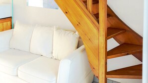 A wooden staircase leading to an upper floor, a white sofa with cushions, and a floor lamp.