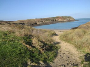 A coastal path leading to a beach with grassy dunes and a rocky outcrop in the distance.
