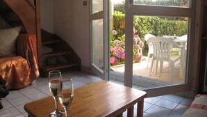 A room with a wooden table, two glasses of white wine, a sofa, and a view of a garden through a glass door.
