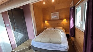 A bedroom with a bed, wooden walls, a door, and two wall-mounted lamps.
