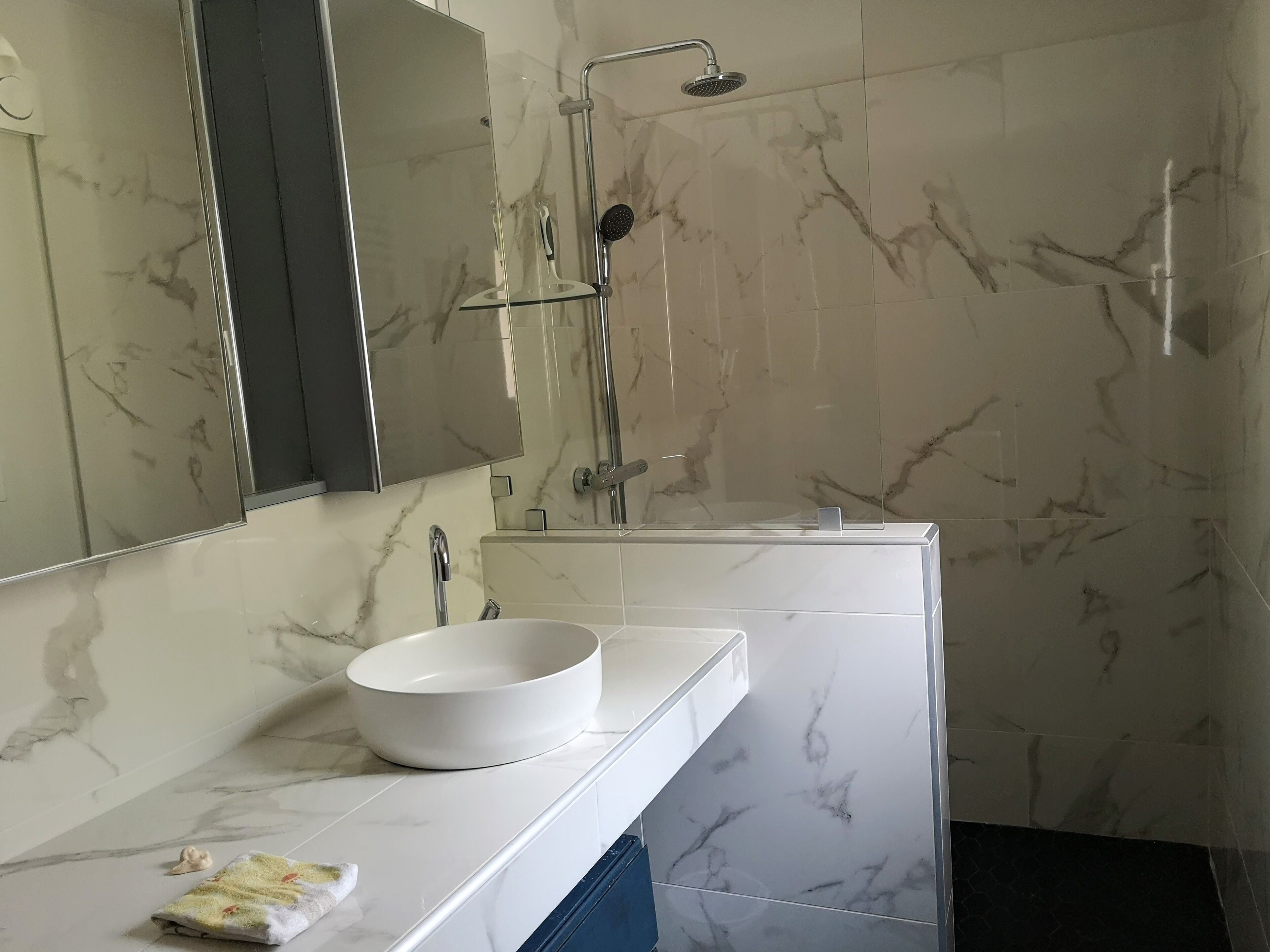 Een moderne badkamer met een wit marmeren wastafel, een douche met glazen wanden en een grote spiegel.