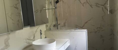 Een moderne badkamer met een wit marmeren wastafel, een douche met glazen wanden en een grote spiegel.