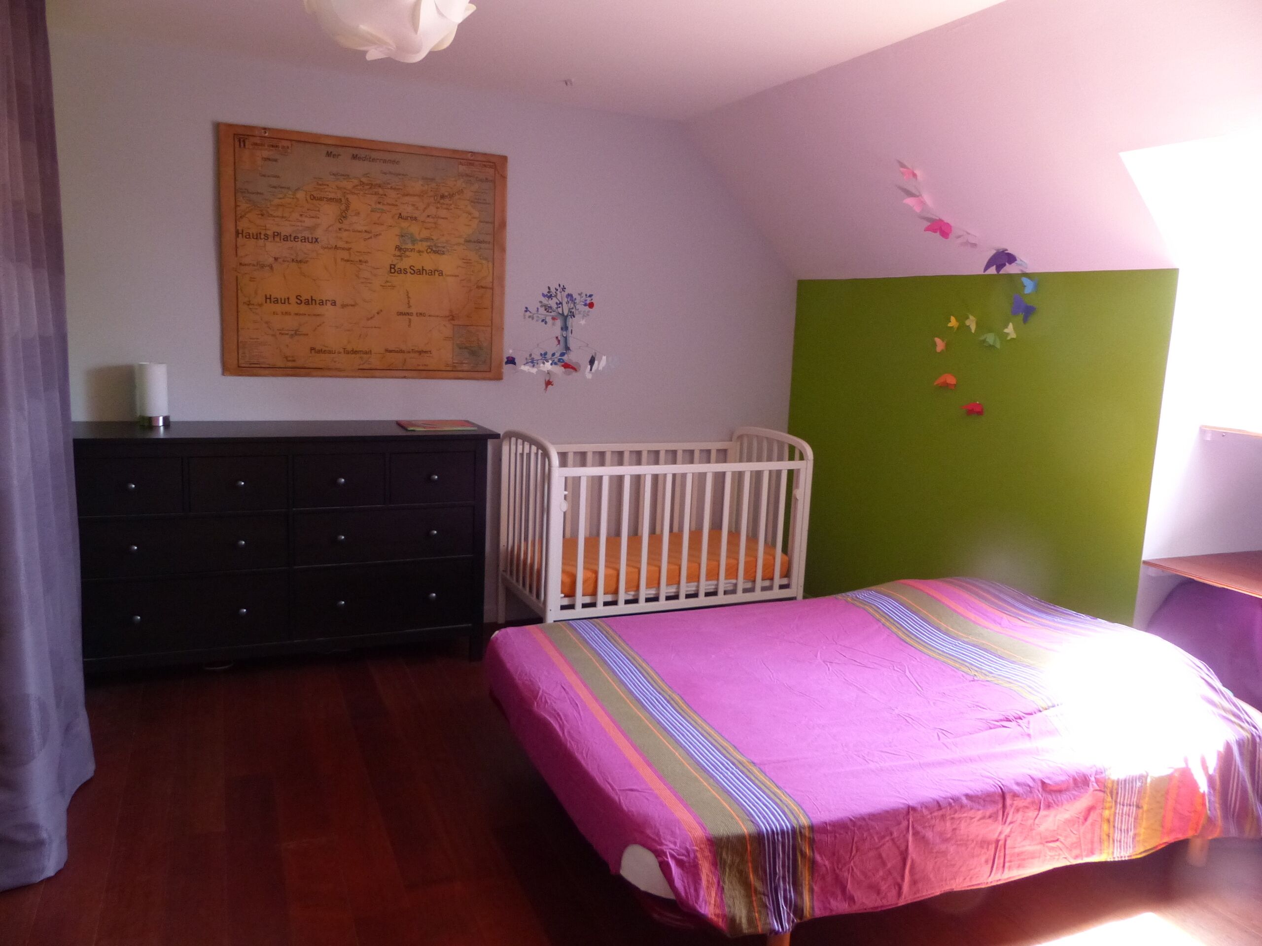 Una stanza con una culla, un comò e un letto con una coperta colorata.