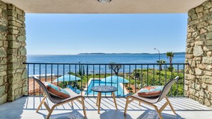En balkon med to stole og et bord, med udsigt over et poolområde og havet.