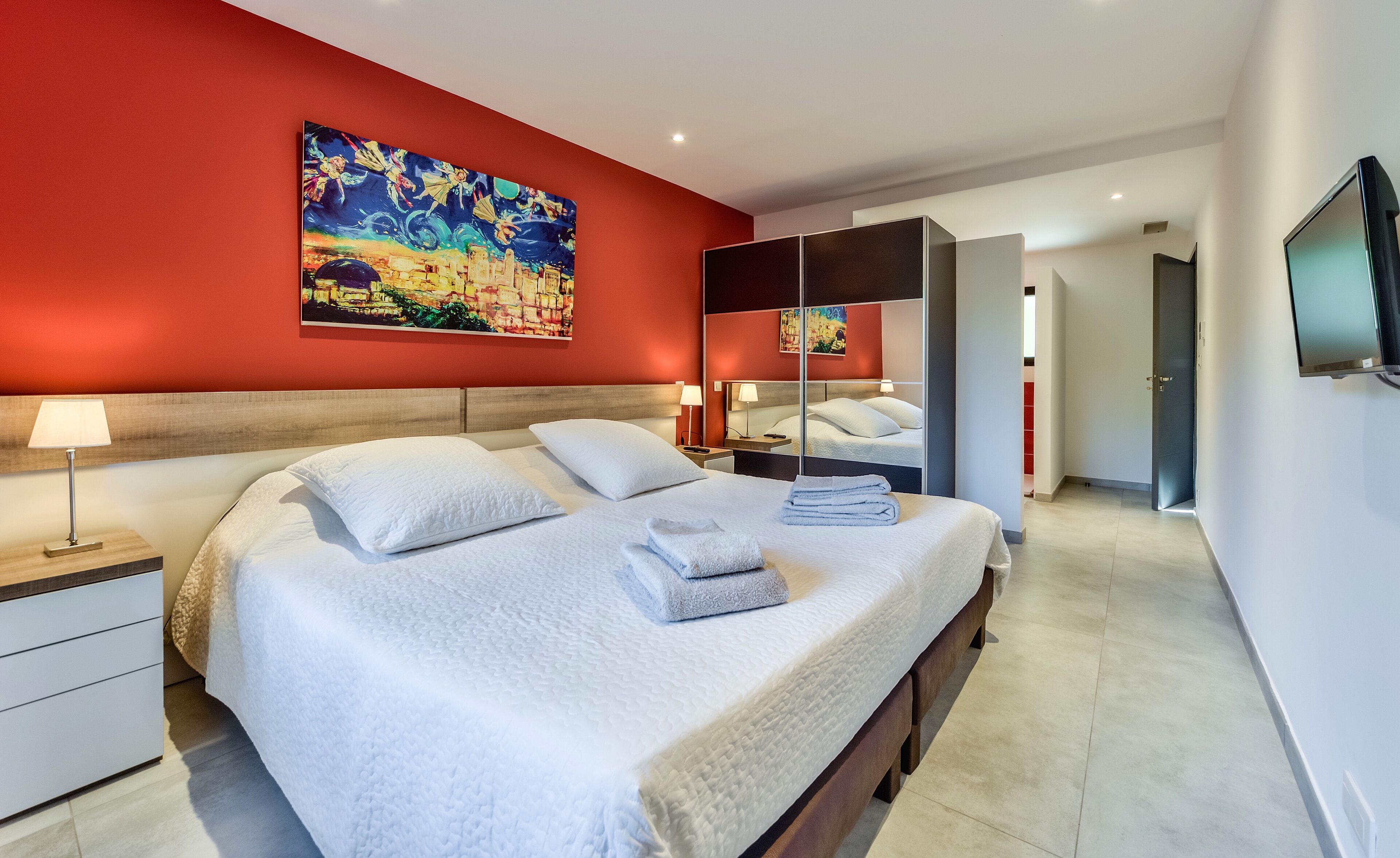 Une chambre d’hôtel avec un grand lit, une table de chevet, une commode, un miroir et un tableau au mur.
