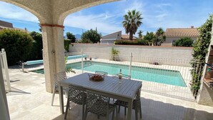 Une terrasse couverte avec une piscine, des sièges d’extérieur et une vue sur le quartier.
