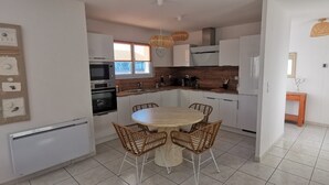 Une cuisine moderne avec des meubles blancs, une table ronde en bois, des chaises en osier et un four encastré.