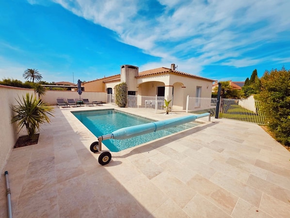 Una piscina con cubierta, sillas de descanso y un área de patio con baldosas.