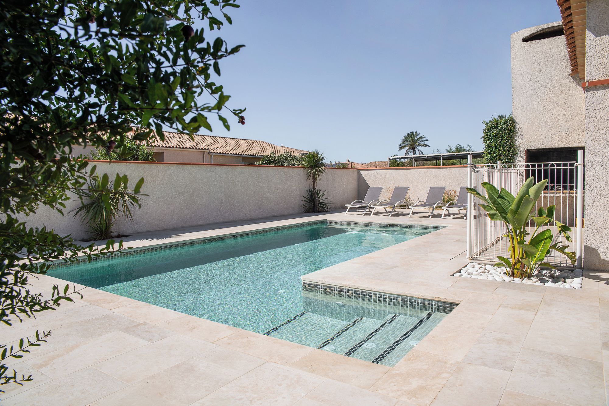 A swimming pool with clear water, surrounded by a tiled deck, and a few lounge chairs.