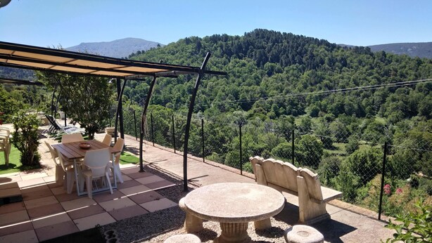 Eine Terrasse im Freien mit einem runden Tisch und Stühlen, umgeben von einer Steinsitzbank und einer Pergola.