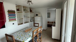 Eine kleine Küche mit weißen Schränken, einer Mikrowelle und einem Kühlschrank. Ein Esstisch mit Stühlen befindet sich vor der Küche.
