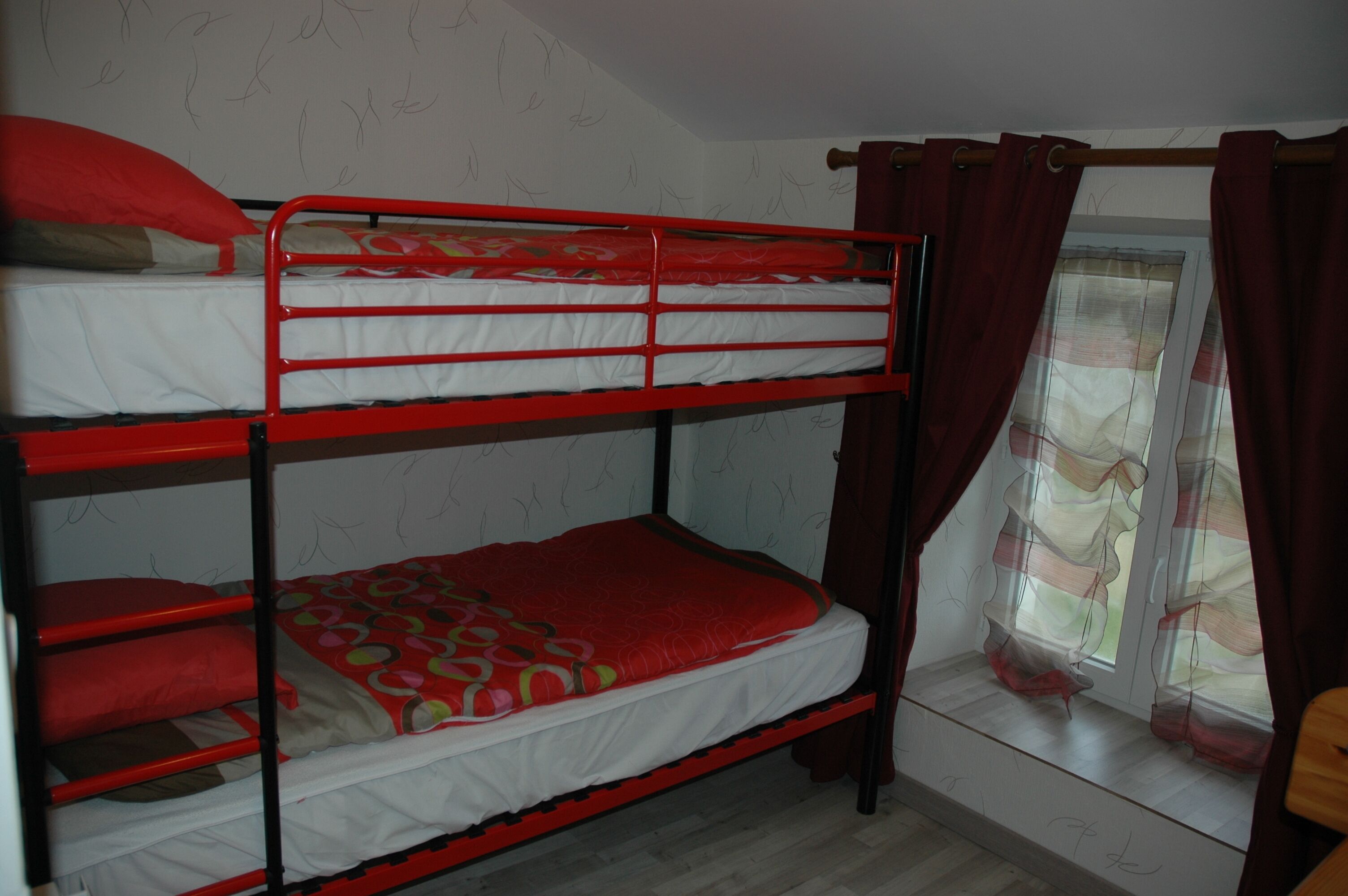 A bunk bed with red railings and a patterned bedspread.