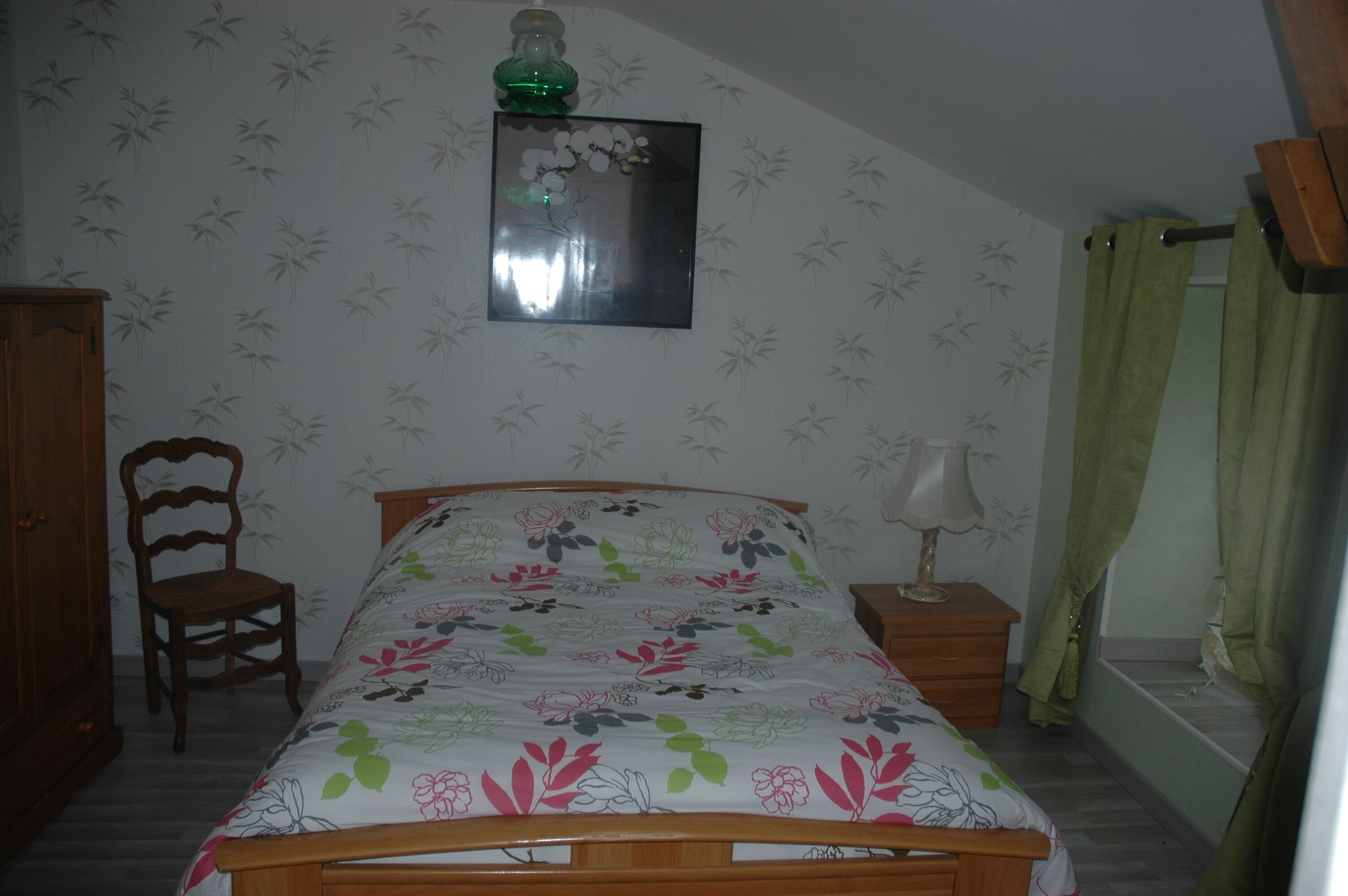 A bedroom with a bed, a chair, a nightstand, a lamp, a mirror, and a wardrobe.