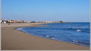 A beach with a clear sky, a sandy shore, and buildings in the background. - Saint pierre home Sea + terrace and panoramic mediterrannée. (Fleury)