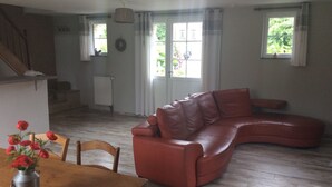 Ett vardagsrum med en brun lädersoffa, ett träbord och en metallvas med röda blommor, samt en trappa som leder upp till ett övre våningsplan.