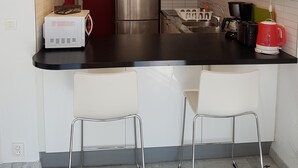 Keittiössä on musta työtaso, valkoiset kaapit, ruostumattomasta teräksestä valmistettu jääkaappi, mikroaaltouuni, vedenkeitin ja kaksi baarituolia.