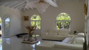 A spacious living room with a white sofa, a glass coffee table, and a chandelier. There are two large windows with arched tops, allowing natural light to enter. - Not to miss! Beautiful and large villa very nice, all comfort and jacuzzi (LE FRANCOIS)