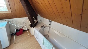 Un baño pequeño y rústico con techo de madera, una bañera blanca, ducha y tendedero.