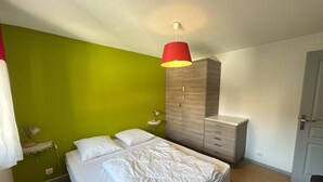 Un dormitorio con cama, armario, mesita de noche con lámpara y pared verde.