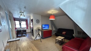 Un espacio habitable compacto con kitchenette, comedor, sofá de cuero rojo, mesita y televisor sobre un mueble.