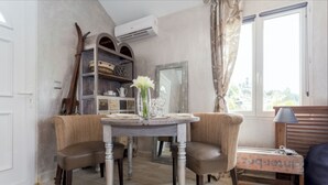 A dining area with a round table, two chairs, a vase with flowers, a bookshelf, and a window with curtains. - Detached house with summer Jacuzzi (May to early October), barbecue. (Nice)