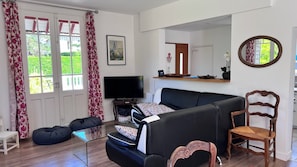 A living room with a sofa, a television, a wooden chair, a glass coffee table, and a large window with curtains. - Norman house, completely renovated, seaside garden, terraces, wifi (Merville-Franceville-Plage)