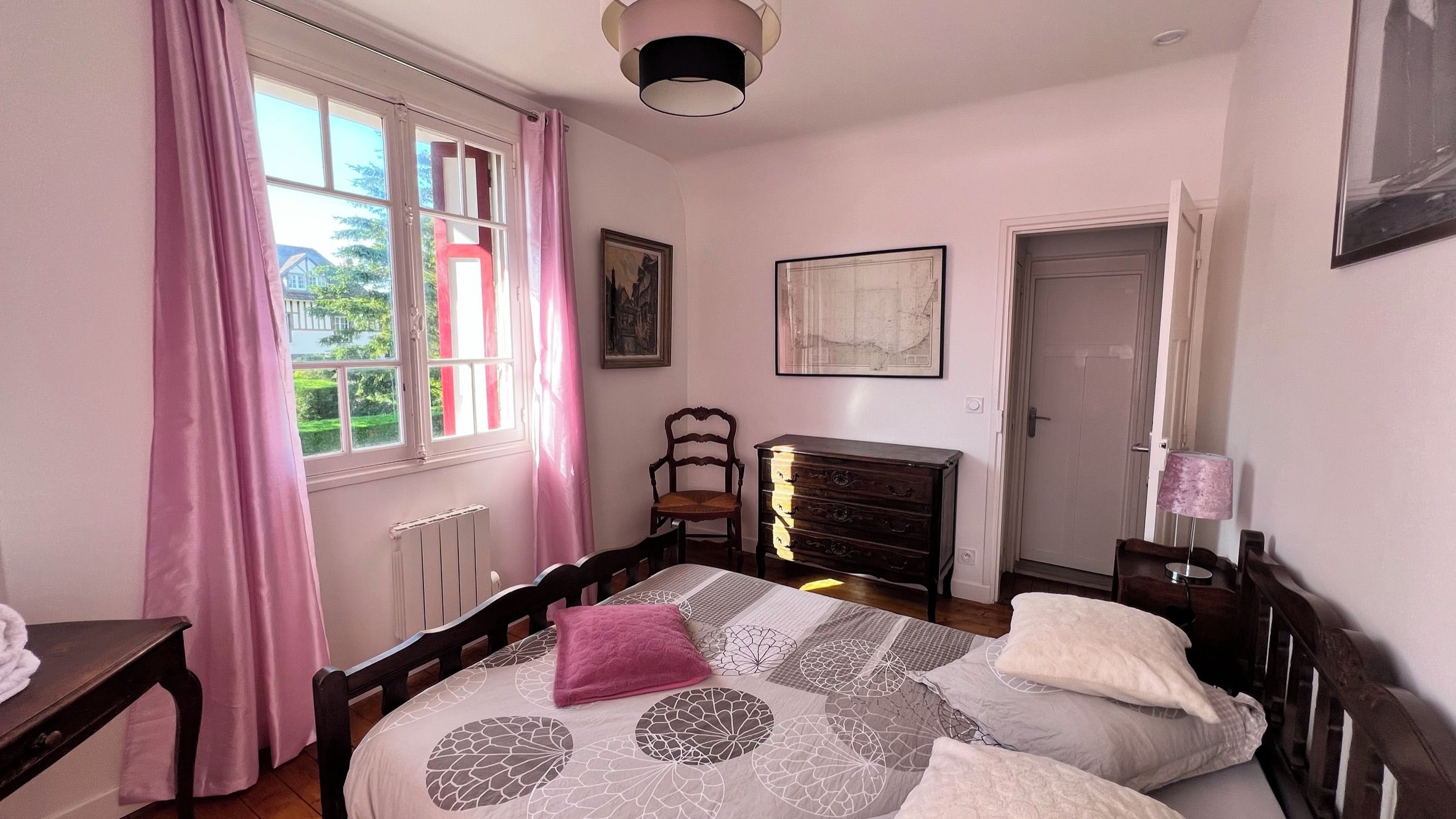 Une chambre à coucher comprenant un lit, une commode, une chaise, un radiateur, une porte et une fenêtre avec des rideaux.
