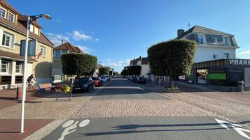 A cobblestone street lined with parked cars and buildings, including a pharmacy.