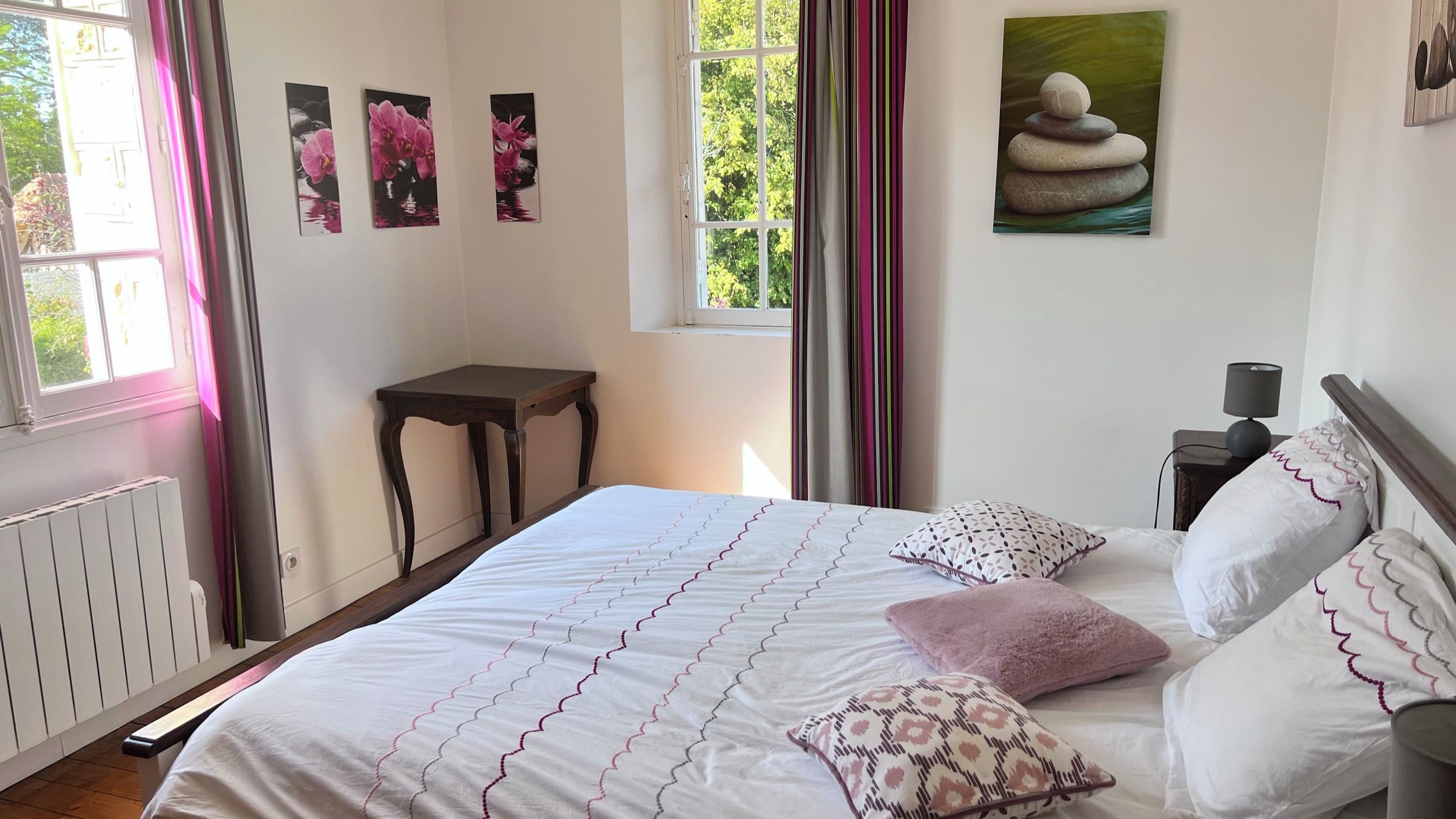 Een slaapkamer met een bed, kussens, een nachtkastje, een lamp en kunst aan de muur.