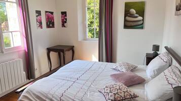 Een slaapkamer met een bed, kussens, een nachtkastje, een lamp en kunst aan de muur.
