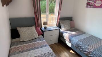 Ein Schlafzimmer mit zwei Einzelbetten, einem Nachttisch mit Lampe und einem Fenster mit Vorhängen.