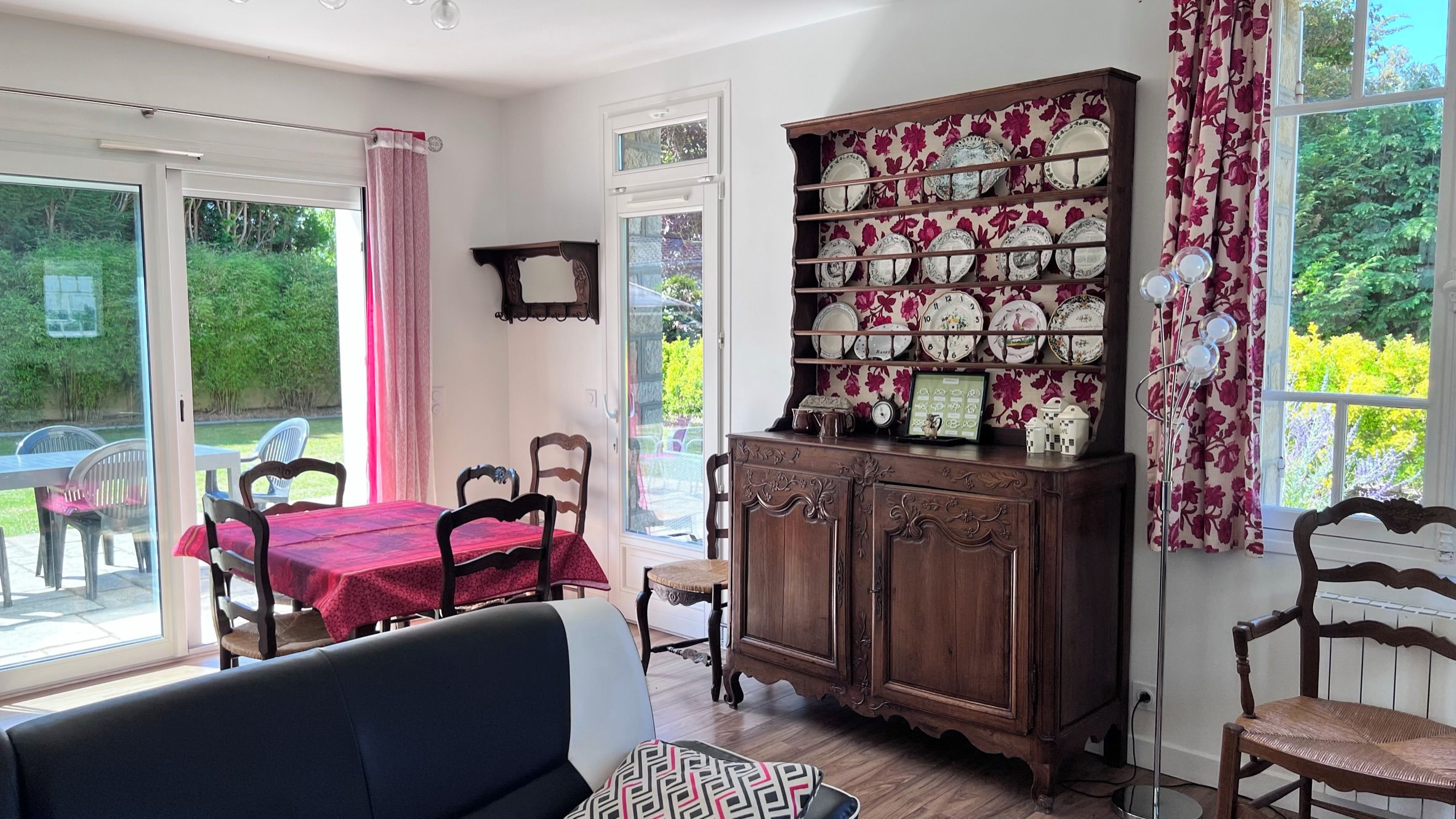 A dining area with a table and chairs, a cabinet with decorative plates, and a view of greenery outside.