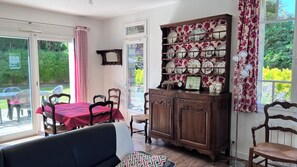 Een eetgedeelte met een tafel en stoelen, een kast met decoratieve borden en uitzicht op groen.