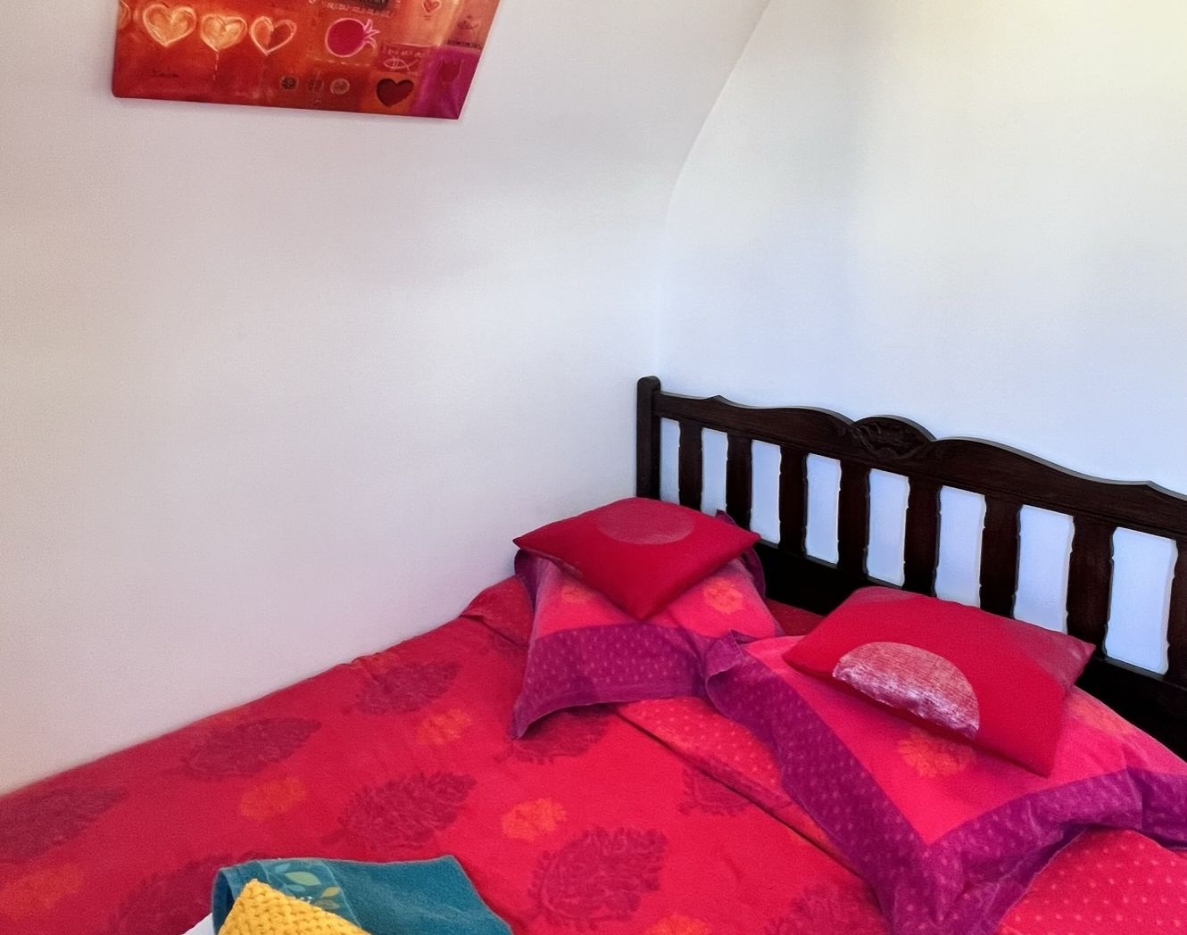 Un lit avec une tête de lit en bois, une literie rouge et un mur orné d’une œuvre d’art sur le thème du cœur.