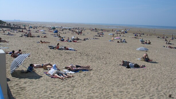 Ein Strand mit Menschen, die in der Sonne liegen und unter Sonnenschirmen entspannen.