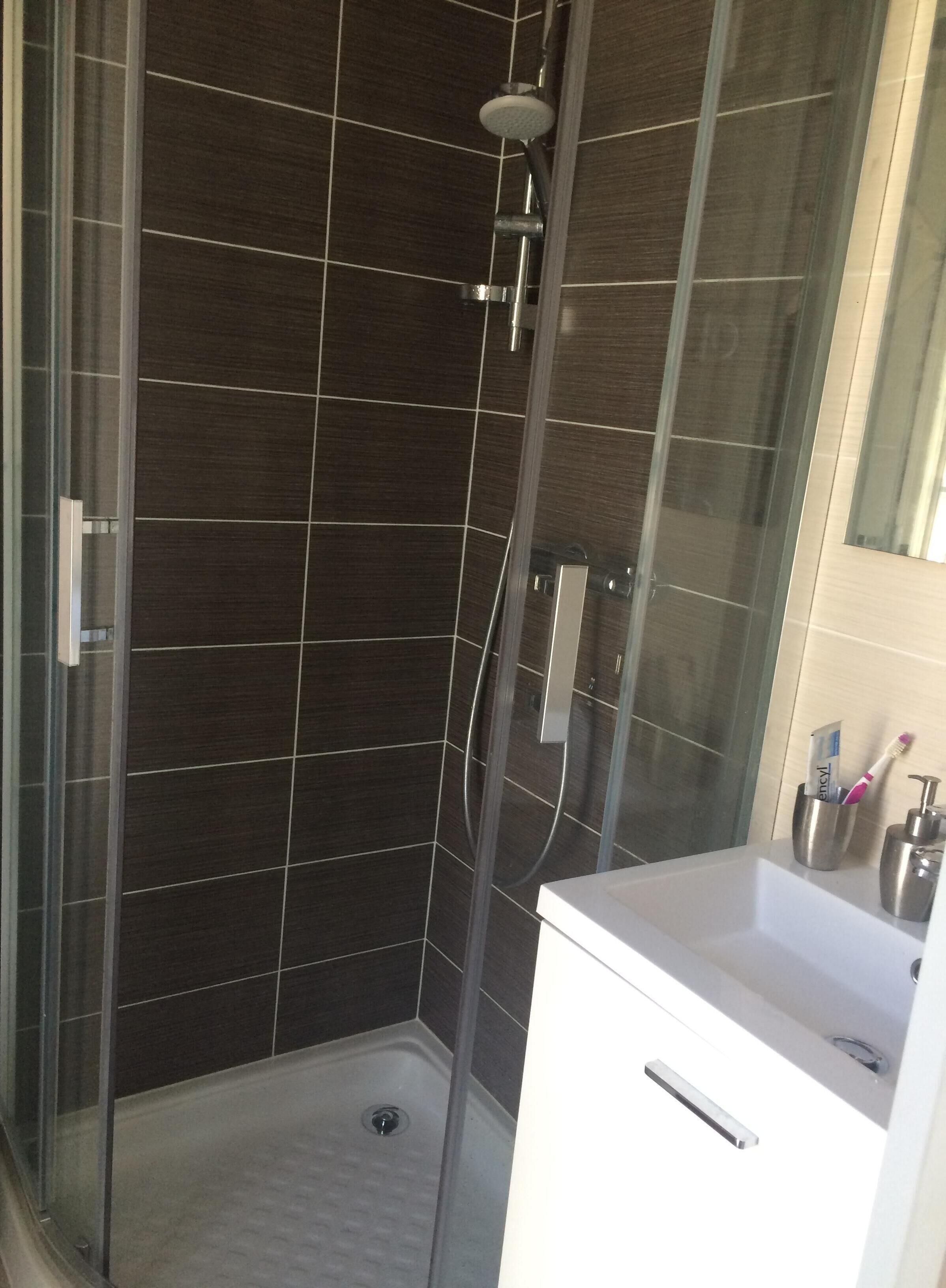 Un bagno moderno con cabina doccia in vetro, pareti rivestite di piastrelle scure e un lavabo bianco con specchio.