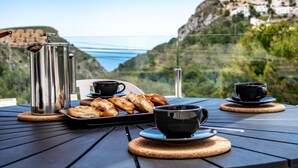 Ein Tisch mit Kaffeemaschine, Tassen und Gebäck, vor einer malerischen Bergkulisse.