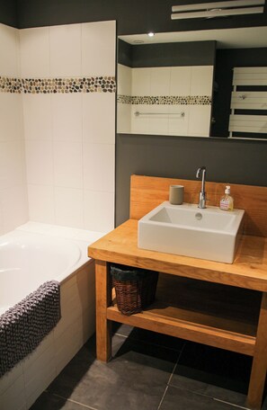 A bathroom with a white bathtub, a wooden vanity with a sink, a mirror, and a tiled backsplash. - Large **** farmhouse renovated in the countryside. (Larodde)
