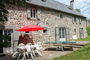 A stone building with a table and chairs under a red umbrella, a ping pong table, and a door. - Large **** farmhouse renovated in the countryside. (Larodde)