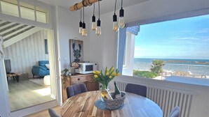 Ein Essbereich mit einem runden Holztisch, vier Stühlen, einer Chandelüster und Blick auf das Meer.