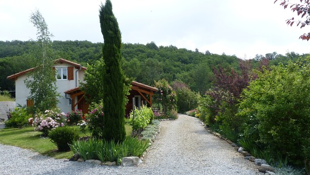 Una casa con vialetto in ghiaia che conduce a un portico in legno, circondata da vegetazione rigogliosa e piante fiorite.