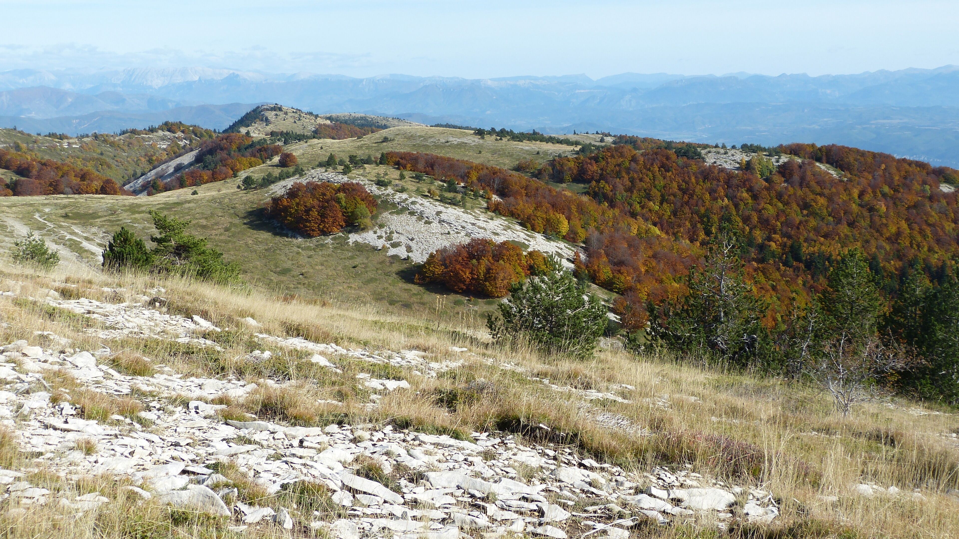 A mountainous landscape with autumn foliage, rocky terrain, and distant mountain ranges.