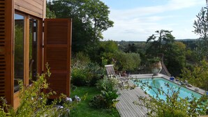 Un jardin avec une terrasse en bois, une piscine et une végétation luxuriante.