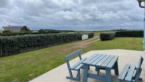 Un patio con banco y mesa, un seto y vista al mar.