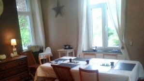 Zona pranzo con tavolo apparecchiato per quattro persone, sedie in legno, un tavolino e una finestra con tende.