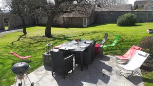 Patio esterno con tavolo in pietra apparecchiato per mangiare, circondato da sedie in vimini e un barbecue.