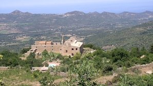 A historic stone building with multiple windows and a courtyard, surrounded by lush greenery and mountains in the background. - LUXURY VILLA with exceptional panoramic views, a pool, and ocean views (Speloncato)