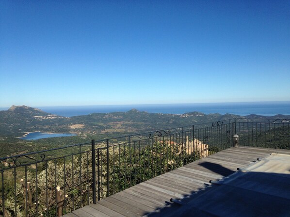 A wooden deck with a metal railing overlooking a mountainous landscape with a clear sky.